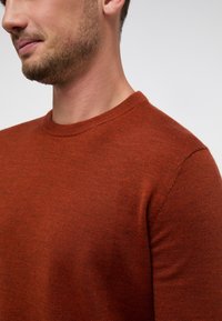 Maglione lavorato a maglia arancione con collo rotondo, maniche aderenti e una texture liscia, che mette in evidenza un design semplice e classico.