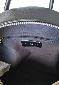 Interno di una borsa in pelle nera con una tasca con zip e foderato in tessuto. Presenta un piccolo tag con logo impresso. Texture liscia e design minimalista.