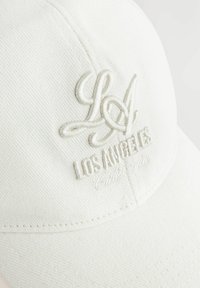 Cappellino da baseball bianco in cotone con ricamo del testo "LA" e "LOS ANGELES California" in filo coordinato, dotato di una superficie in tessuto testurizzato.