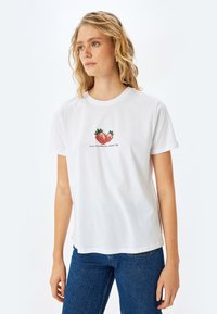 Hvid bomulds t-shirt med et farverigt jordbærmotiv og teksten "saftig og lækker, naturens kys." Korte ærmer, løs pasform.