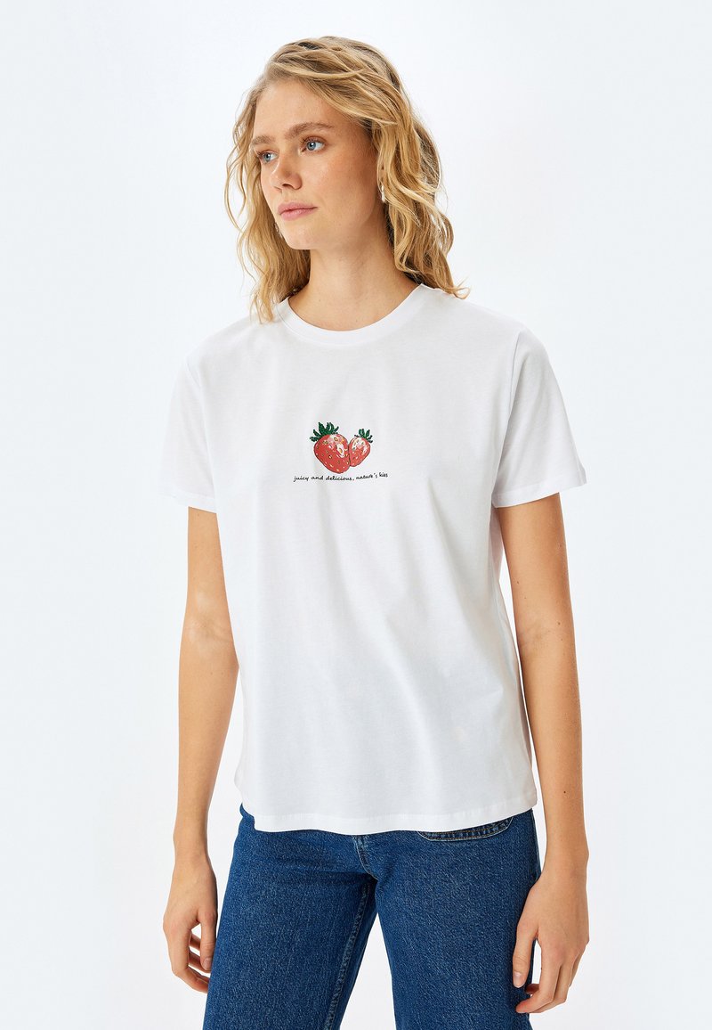 Hvid bomulds t-shirt med et farverigt jordbærmotiv og teksten "saftig og lækker, naturens kys." Korte ærmer, løs pasform.