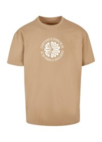 Beige bomulds t-shirt med korte ærmer og rund udskæring. Centreret grafisk design med hvid tekst: "Alt kommer til at gå godt" i et cirkulært mønster.