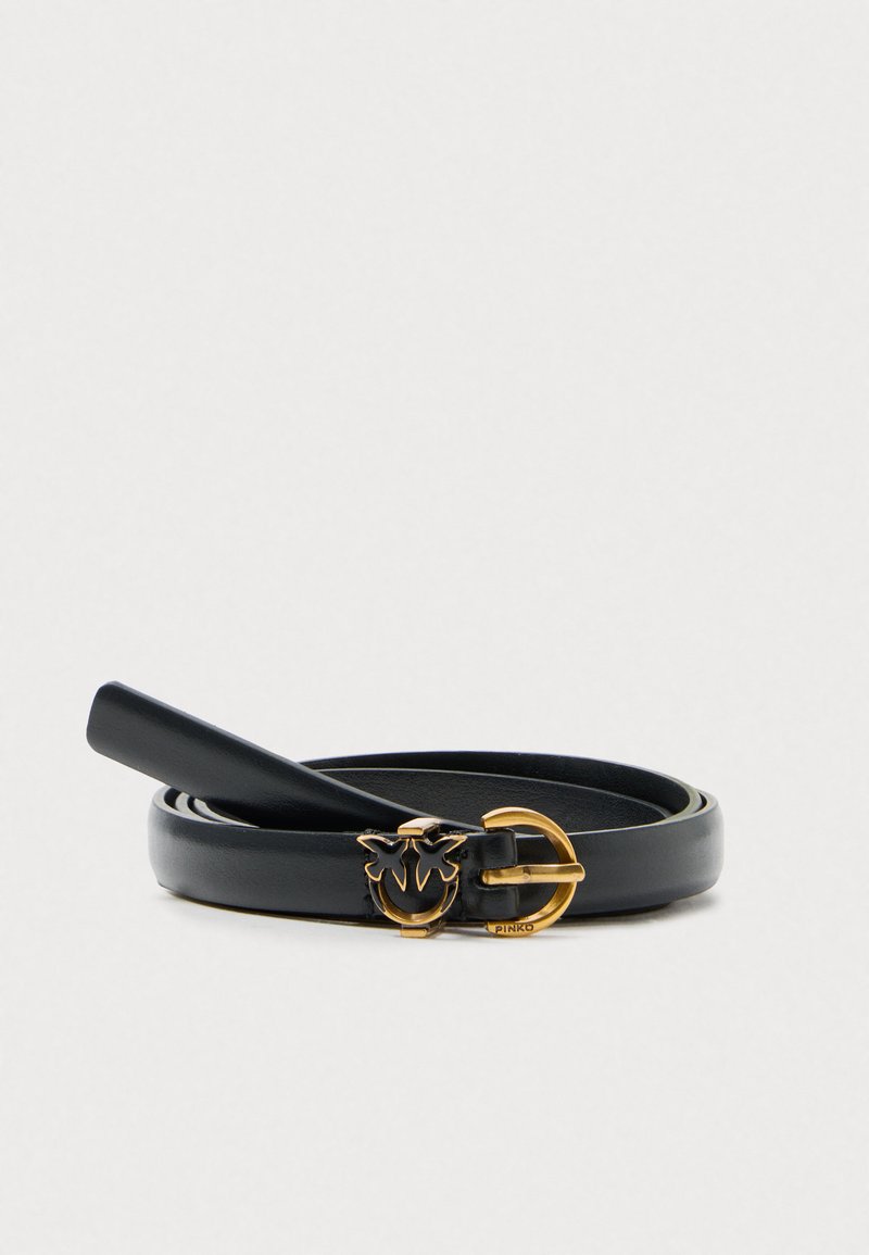 Črn usnjeni pas z ožjo zasnovo, ki ima zlat zaključek z dekorativnim emblemom in sijočo površino.