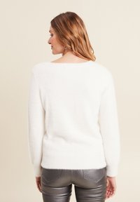 Weißer, flauschiger Pullover mit weitem Halsausschnitt, taillierter Form und langen Ärmeln, getragen mit metallisch silbernen, engen Hosen.