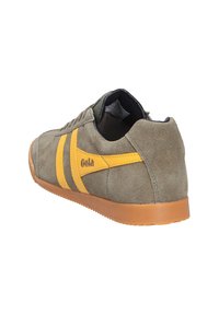 Baskets en daim vert olive avec des rayures jaunes, une semelle en caoutchouc et un design à lacets, vues de l'arrière sur le côté.