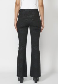 Pantalones acampanados negros con un patrón floral, que presentan una textura suave, bolsillos traseros y acentos metálicos en la cintura.