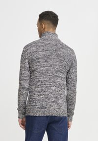 Pletena sweatshirt u sivoj i tamnoplavoj boji s visokim ovratnikom, s teksturiranim uzorkom i rebrastim manžetama i rubom. Pogled sa stražnje strane prikazuje prilagođen dizajn.
