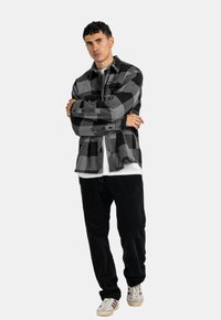 Schwarz-graues kariertes Flanellhemd mit zwei Brusttaschen, kombiniert mit schwarzen Cordhosen und beigen Sneakern mit roten Streifen.