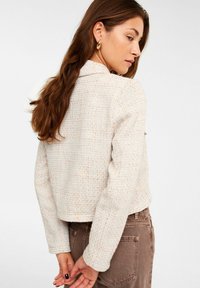 Blazer in lichtbeige textuurstof met subtiele oranje spikkels, voorzien van een kraag, taps toelopende mouwen en een verkorte stijl.