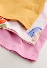 Trois tissus en coton pliés : jaune moutarde, blanc avec des formes abstraites colorées, et rose uni, présentés en gros plan.