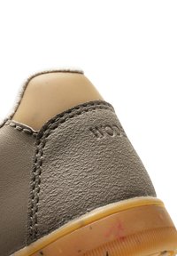 Grå sneakersko med texturerat läder, kontrasterande gummisul och ljusfärgad vaddering. Sytt detaljer runt överdelen.