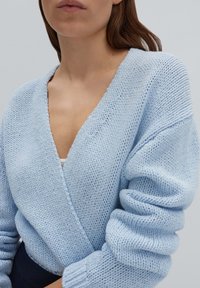 Cardigan en tricot bleu clair avec un décolleté en V profond, des manches amples et une finition texturée ; présente un design enveloppant et une coupe décontractée.