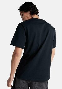 Camiseta de algodón negra con cuello redondo y mangas cortas. Presenta un ajuste relajado y una textura suave, mostrada desde la parte de atrás.