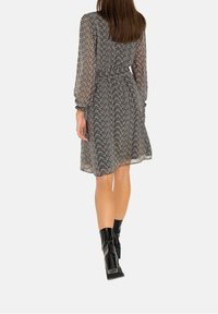 Vestido de patrones en blanco y negro con mangas largas, cintura ceñida y falda fluida, combinado con botas de tacón negras.