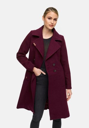 Manteau en laine mélangée bourgogne avec un devant croisé, un large col à revers et des poches latérales, porté sur un haut noir et un jean sombre.
