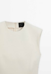 Haut sans manches beige avec encolure ronde et fermeture éclair au dos, étiqueté "Massimo Dutti Studio", présenté sur fond blanc.