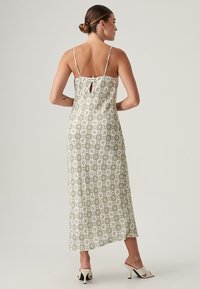Abito maxi di un verde chiaro con un motivo floreale e geometrico. Presenta spalline sottili, una schiena a fessura e una silhouette svasata.