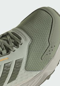 Grüner Sportschuh mit strukturiertem Mesh-Obermaterial, synthetischen Überzügen und gemusterter Sohle. Schnürsenkel in passendem Grün mit dezentem Markenlogo.