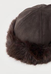 Καφέ σκούρο καπέλο σουέντ με απαλό, αφράτο γούνινο περίβλημα γύρω από τις άκρες, πάνω σε λευκό μονόχρωμο φόντο.