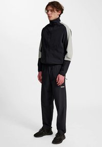 Marinblå träningsdräkt med ljusgrå detaljer. Zip-up jacka med hög krage och fickor; matchande byxor med elastisk midja, smal passform och logotypdetalj.