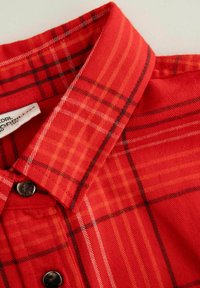 Czerwona koszula w kratę z teksturowanej tkaniny, z zapięciem na guziki i klasycznym kołnierzykiem, w którym w ramach wzoru występują kontrastowe czarne i białe linie.