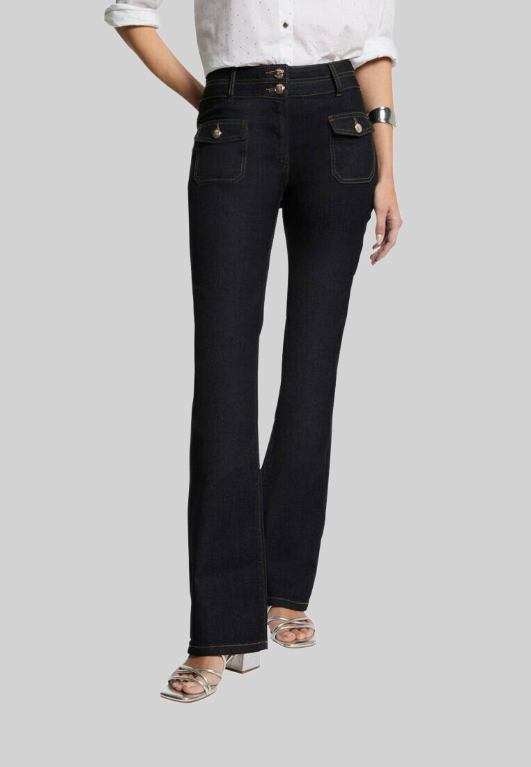 Jeans a zampa d'elefante in denim blu scuro con tasche frontali, chiusura a due bottoni e accenti di cucitura dorata. Il modello indossa scarpe alla caviglia.