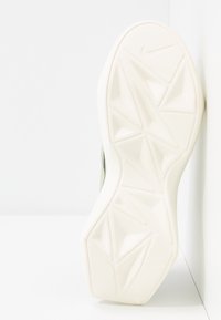 Semelle extérieure de chaussure de sport blanche présentant un motif de bande de roulement géométrique et le logo Nike. Le talon est arrondi avec une finition lisse et texturée.