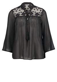 Zwarte blouse met lange mouwen, doorschijnende stof, ingewikkelde bloemborduursels op de schouderpartij en een bijpassende striksluiting bij de hals.