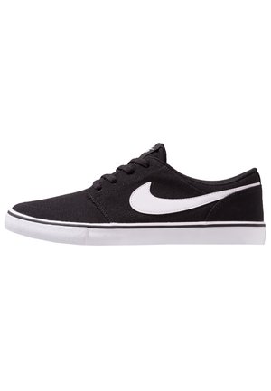 Baskets basses noires avec un swoosh Nike blanc, des lacets noirs et une semelle en caoutchouc blanche avec une bande noire.