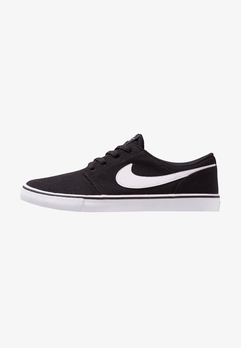Baskets basses noires avec un swoosh Nike blanc, des lacets noirs et une semelle en caoutchouc blanche avec une bande noire.