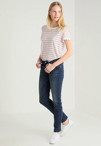 Striped short-sleeve top with scalloped sleeves, paired with dark blue skinny jeans and white sneakers. Simple design with a casual fit.