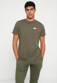 Ελαιόχρωμο βαμβακερό μπλουζάκι με κοντά μανίκια και ένα μικρό μπλε, κόκκινο και λευκό λογότυπο στο αριστερό στήθος. Λείο ύφασμα, σχέδιο με κωπηλατική λαιμόκοψη.