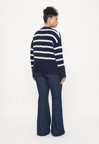 Μπλέι ναυτικού και λευκή ριγέ μπλούζα με πλέξη, συνδυασμένη με καμπάνα σκούρες τζιν παντελόνες. Πλεκτό υλικό, άνετη εφαρμογή και μακριά μανίκια.