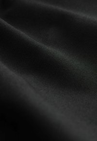 Zwarte stof met een gladde textuur, voorzien van een subtiel ribbelpatroon. Gefotografeerd vanuit een bepaalde hoek, waarbij plooien en lichtreflectie zichtbaar zijn.