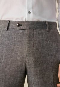 Sive hlače s teksturom i uskim krojem, koje imaju zatvaranje na dugme i diskretne nabore na prednjem dijelu za dodatni detalj, napravljene od laganog materijala.