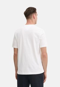 T-shirt bianca in cotone con maniche corte e colletto rotondo, caratterizzata da un design semplice senza motivi o accenti, mostrata dal retro.