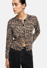 Kardigan w leopardzie w kolorze brązowym, kremowym i czarnym. Posiada okrągły dekolt, zapięcie na guziki i dopasowany krój. Teksturowany materiał dzianinowy.