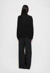 Čierny oversized sveter s vysokým golierom, skombinovaný s voľnými tmavými nohavicami. Mäkká textúra, minimalistický dizajn, bez viditeľných vzorov.