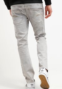Jeans de mezclilla gris claro con un ajuste estrecho, que cuentan con dos bolsillos traseros y detalles sutiles de costura, combinados con zapatillas blancas.