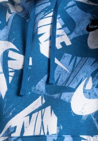 Modrá mikina s kapucí s bílými grafickými logy, s texturovanou úpravou, kapucí se stažením a žebrovaným lemem. Loga se liší velikostí a orientací.