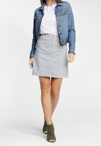 Chaqueta de mezclilla con dos bolsillos en el pecho, una falda de mezclilla a rayas gris claro con botones en el frente, y botas abiertas hasta el tobillo en color oliva.