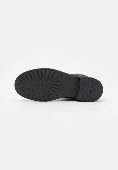 Suela de bota de goma negra con patrones de relieve texturizados para mayor agarre, con sutiles marcas y un diseño de tacón plano.