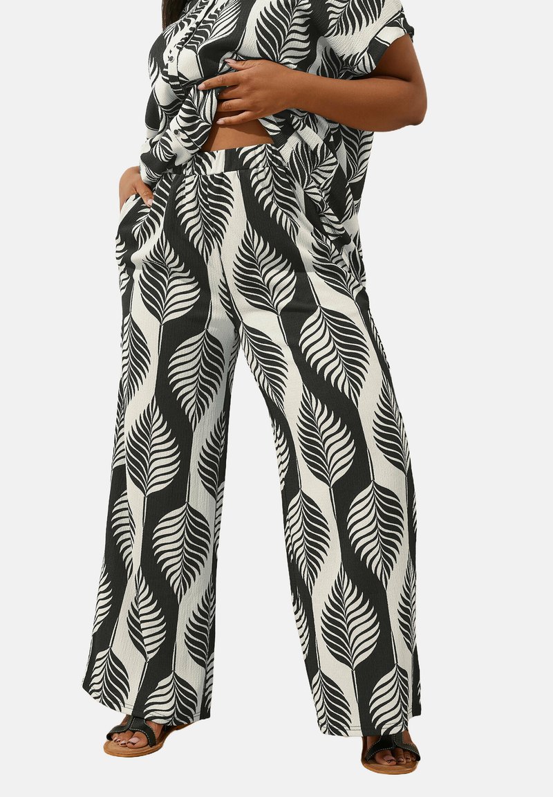 Haut à motifs de feuilles en noir et blanc et pantalon large en tissu léger, avec une coupe ample et des poches latérales. Des sandales marron complètent le look.