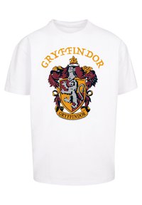Fehér póló Gryffindor címerével, élénk színekkel, egy oroszlánnal és díszes részletezéssel, a "GRYFFINDOR" névvel a címer fölött.