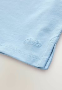 Ljusblå bomullströja med rundad krage, korta ärmar och diskret broderad "Clarks"-logotyp vid fållen. Slät textur och rena sömmar.
