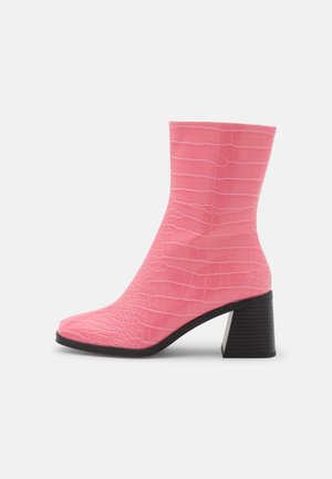 Bottine rose à texture embossée effet crocodile, avec un bout pointu et un talon noir épais. Matière supérieure lisse et design élégant.