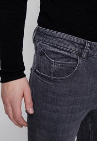 Vaqueros de mezclilla gris con un corte ajustado, que cuentan con un diseño clásico de cinco bolsillos, costuras visibles y un sutil desgaste en la tela.