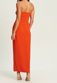Langes, trägerloses Abendkleid aus leuchtend orangefarbenem Stoff. Das Design verfügt über ein tailliertes Oberteil und einen geraden Rock. Klare, hochhackige Sandalen.
