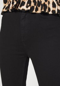 Jeans de mezclilla negra con un diseño ajustado, que cuentan con un bolsillo frontal y detalles de costura sutiles, combinados con una blusa de peplum de estampado de leopardo.