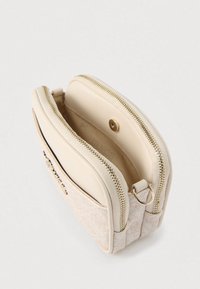 Kompakt bézs válltáska két cipzáras rekesszel, arany színű fém részletekkel és díszes első zsebbel.